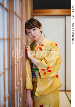 一位身穿和服的年輕女子站在日式房間的障子門旁。 134614223