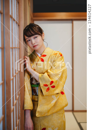 一位身穿和服的年輕女子站在日式房間的障子門旁。 一位身穿和服的年輕女子站在日式房間的障子門旁。 134614227