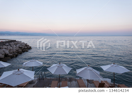 Peaceful seaside view in Croatia with umbrellas and sunbeds by the Adriatic Sea at sunset. Seaside view in Croatia with white parasols and wooden sunbeds at sunset, overlooking the calm Adriatic Peaceful seaside view in Croatia with umbrellas and sunbeds by the Adriatic Sea at sunset. Seaside view in Croatia with white parasols and wooden sunbeds at sunset, overlooking the calm Adriatic 134614234