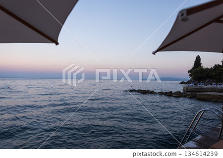 Romantic seaside evening in Croatia with peaceful waves, umbrellas, and a pastel sunset sky Peaceful seaside view in Croatia by the Adriatic Sea at sunset. Relaxing summer holiday scene Romantic seaside evening in Croatia with peaceful waves, umbrellas, and a pastel sunset sky Peaceful seaside view in Croatia by the Adriatic Sea at sunset. Relaxing summer holiday scene 134614239