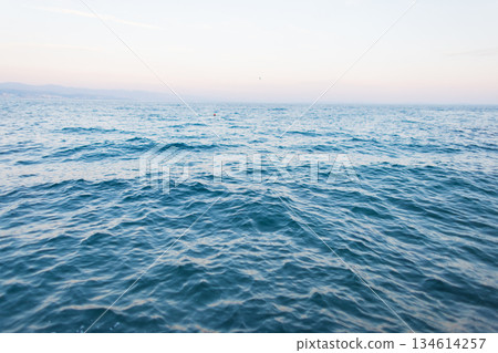 Calm blue sea with gentle waves under a clear sky at sunset. Minimal seascape background symbolizing peace, freedom. Blue ocean surface with calm waves fading into the horizon. Natural seascape 134614257