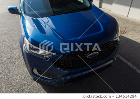 Modern blue SUV parked on city street with sunlight reflections on shiny surface and contemporary design details. 134614294