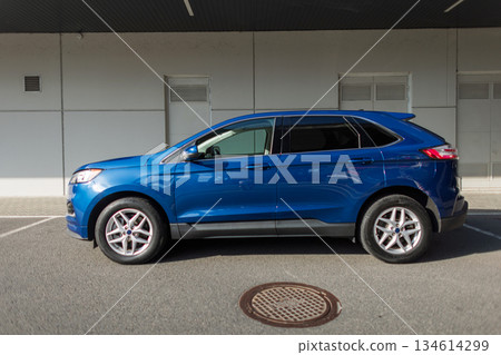 Side profile of blue SUV car parked on asphalt near building facade. Compact modern vehicle for city and travel. Compact family SUV in bright blue paint, parked on city parking lot. Side profile of blue SUV car parked on asphalt near building facade. Compact modern vehicle for city and travel. Compact family SUV in bright blue paint, parked on city parking lot. 134614299