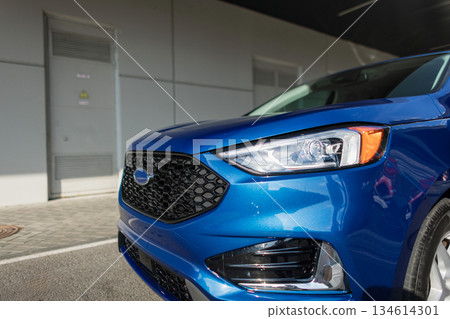 Close-up of a blue SUV front with shiny headlights and hexagon grille, urban background. Close-up of a blue SUV front with shiny headlights and hexagon grille, urban background. 134614301