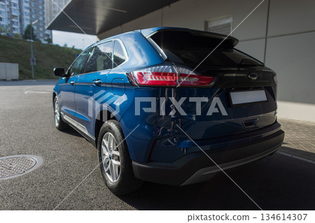 Stylish blue crossover vehicle outdoors, urban architecture background. Sleek blue car parked near concrete structure, rear lights visible. Stylish blue crossover vehicle outdoors, urban architecture background. Sleek blue car parked near concrete structure, rear lights visible. 134614307