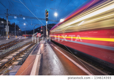 Blurred red passenger train passing mountain railway station Blurred red passenger train passing mountain railway station 134614393