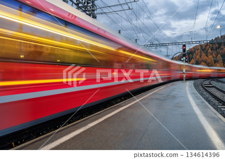 Blurred red passenger train passing mountain railway station Blurred red passenger train passing mountain railway station 134614396