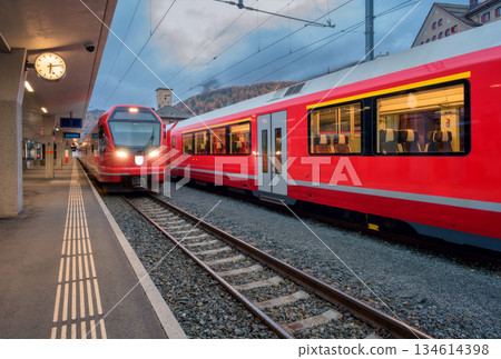 Red modern trains on mountain railway station in Swiss Alps. Dusk Red modern trains on mountain railway station in Swiss Alps. Dusk 134614398