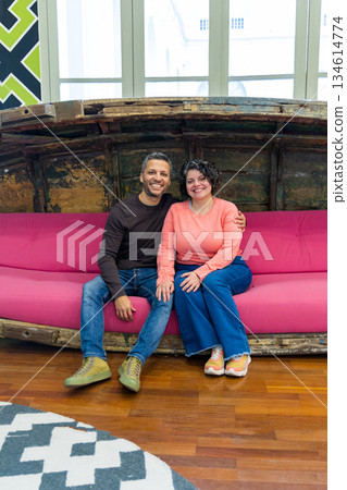 A man and a woman are sitting on a pink couch A man and a woman are sitting on a pink couch 134614774