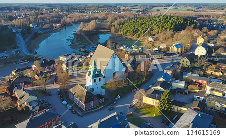 Porvoo, Finland - December 08, 2020: Aerial perspective of a picturesque village featuring a historic church and winding river, surrounded by lush greenery and colorful houses Porvoo, Finland - December 08, 2020: Aerial perspective of a picturesque village featuring a historic church and winding river, surrounded by lush greenery and colorful houses 134615169