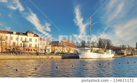 Porvoo, Finland - December 08, 2020: Historic ship is docked by the waterfront, surrounded by buildings and trees, under a clear blue sky with wispy clouds Porvoo, Finland - December 08, 2020: Historic ship is docked by the waterfront, surrounded by buildings and trees, under a clear blue sky with wispy clouds 134615172