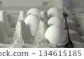 A close-up view of fresh white eggs nestled in a cardboard carton, showcasing their smooth texture and subtle shadows, creating a serene and minimalist atmosphere in the composition 134615185