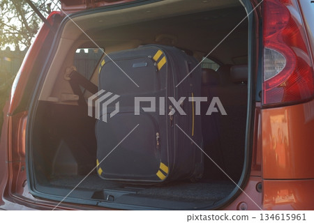Large black suitcase with yellow accents standing upright inside the trunk of an orange car, ready for a trip. 134615961