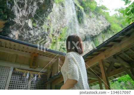 A woman looks up at the waterfall and shrine 134617097