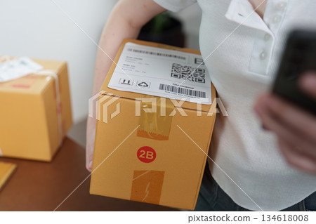 Small Business. Woman scanning package with smartphone for inventory management. 134618008