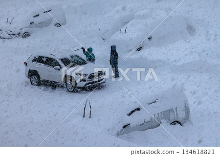 A worker removing snow from a car in heavy snow 134618821
