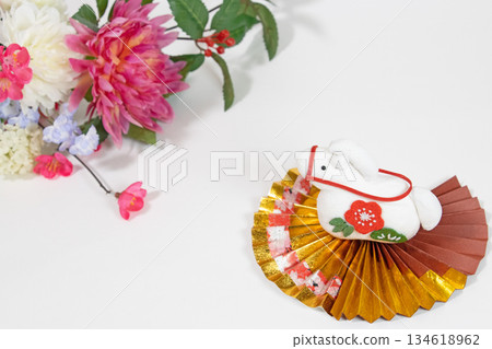 A crepe white horse figurine on a gold fan and New Year's flowers A crepe white horse figurine on a gold fan and New Year's flowers 134618962