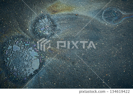 Colorful Oil Slick on Asphalt Shows Circular Patterns and Textures in a City Street During Daylight 134619422