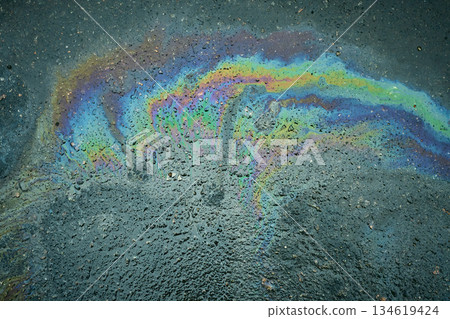 A puddle of gasoline shimmers with bright rainbow reflections on dark asphalt A puddle of gasoline shimmers with bright rainbow reflections on dark asphalt 134619424