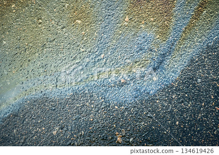 An oil slick, shimmering with vibrant hues, creates an abstract texture on wet asphalt. An oil slick, shimmering with vibrant hues, creates an abstract texture on wet asphalt. 134619426