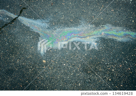 An iridescent puddle of gasoline, reflecting vibrant colors on the rich texture of dark asphalt. 134619428