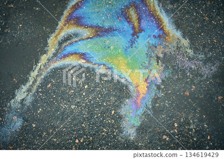 A vibrantly colored oil slick creates an artistic texture on wet asphalt. 134619429