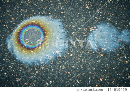 Colorful Oil Slick on Asphalt Surface Shows Vivid Patterns and Textures From Vehicle Leakage Under Cloudy Sky 134619439