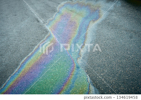 Oil slick creating an iridescent rainbow pattern on dark asphalt, symbolizing pollution Oil slick creating an iridescent rainbow pattern on dark asphalt, symbolizing pollution 134619458