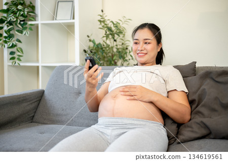 Pregnant asian woman with bare belly looking at a glucose testing kit after using for self exam. 134619561