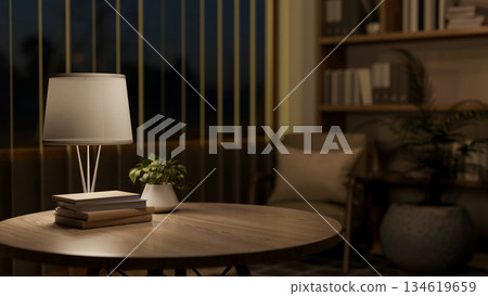 Books and potted plant on wooden round table under lamp light in a living room or a library at night. 134619659