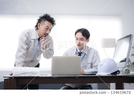 Two businessmen in work clothes talking while looking at a computer. DX and IT in the manufacturing industry. Thinking. Hands on chin. Two businessmen in work clothes talking while looking at a computer. DX and IT in the manufacturing industry. Thinking. Hands on chin. 134619678