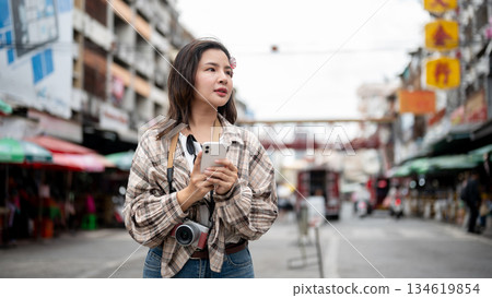 Asian tourist woman looking confused as holding phone with both hands standing by the road in market Asian tourist woman looking confused as holding phone with both hands standing by the road in market 134619854