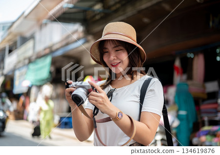 Asian woman wearing hat smiling while holding camera checking photos taken at the local old market. 134619876