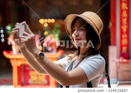 Asian woman wearing hat holding smartphone with both hands taking photo in the Chinese shrine temple Asian woman wearing hat holding smartphone with both hands taking photo in the Chinese shrine temple 134619887