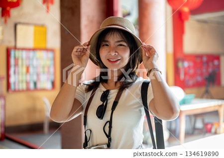 Asian tourist woman touching hat with both hand and looking into camera in the Chinese shrine temple 134619890
