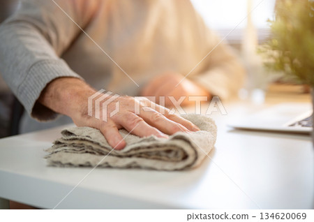 Close up of old white caucasian man hand holding a cloth rag cleaning or wiping dust on white table. Close up of old white caucasian man hand holding a cloth rag cleaning or wiping dust on white table. 134620069