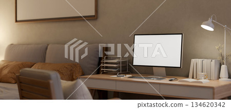 White screen computer with books and lamp aside on wooden table and armchair in a dim lit bedroom. White screen computer with books and lamp aside on wooden table and armchair in a dim lit bedroom. 134620342