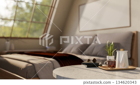 A grey bed with pillow and comforter and iced coffee and kettle atop marble table under roof window. 134620343