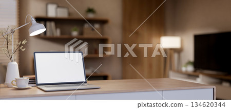 White screen laptop and a coffee cup with vase aside on wooden table under lamp light in living room 134620344