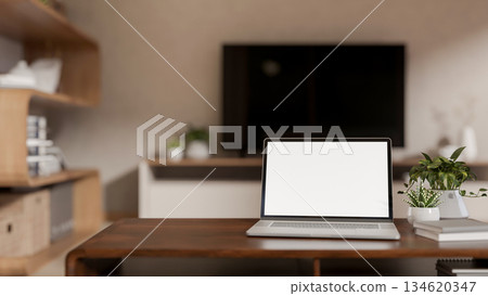 Blank screen laptop and books with potted plants aside on wooden table in a living room or bedroom. 134620347