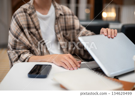 Close up of a man hands closing or opening laptop lid with phone and notebook sitting at cafe table. Close up of a man hands closing or opening laptop lid with phone and notebook sitting at cafe table. 134620499