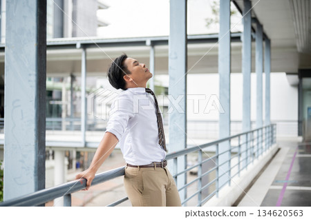Businessman or office worker standing and leaning with both hands on pedestrian footbridge's railing Businessman or office worker standing and leaning with both hands on pedestrian footbridge's railing 134620563