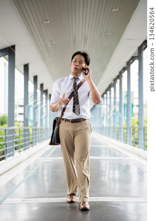 Businessman or office worker talking happily on his phone while walking on a pedestrian footbridge 134620564
