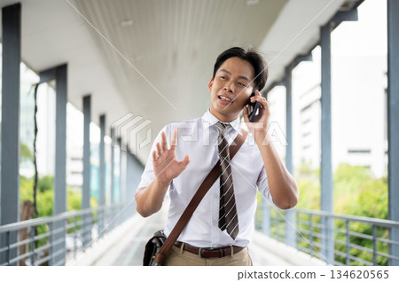Businessman or office worker talking on phone walking with one hand raising on pedestrian footbridge. Businessman or office worker talking on phone walking with one hand raising on pedestrian footbridge. 134620565