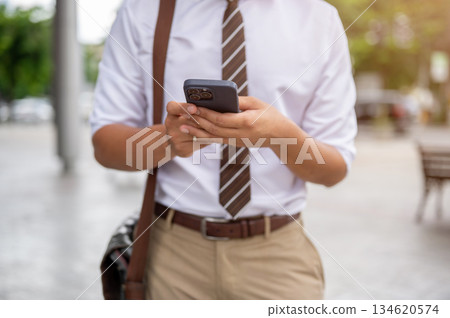 Close up of a male office worker's hands holding and typing on his smartphone while standing in park Close up of a male office worker's hands holding and typing on his smartphone while standing in park 134620574