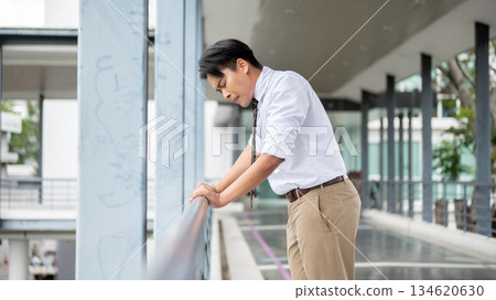 Businessman or office worker holding a railing with both hand looking down on pedestrian footbridge. Businessman or office worker holding a railing with both hand looking down on pedestrian footbridge. 134620630