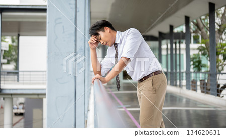 Businessman or office worker holding temple leaning with elbow on a pedestrian footbridge's railing. Businessman or office worker holding temple leaning with elbow on a pedestrian footbridge's railing. 134620631