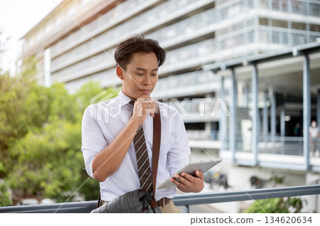 Businessman or office worker hand under chin looking at tablet as standing on pedestrian footbridge 134620634