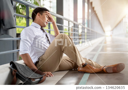 Businessman or office worker holding temple sitting leaning against pedestrian footbridge's railing 134620635