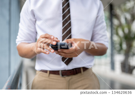 Close up of businessman or office worker touching on smartphone standing on a pedestrian footbridge. Close up of businessman or office worker touching on smartphone standing on a pedestrian footbridge. 134620636